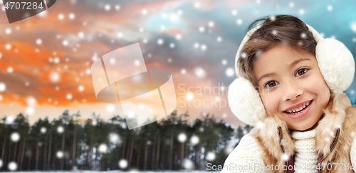 Image of happy little girl in earmuffs over winter forest