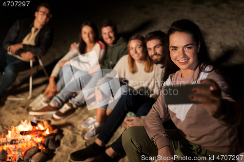 Image of happy friends taking selfie at camp fire on beach