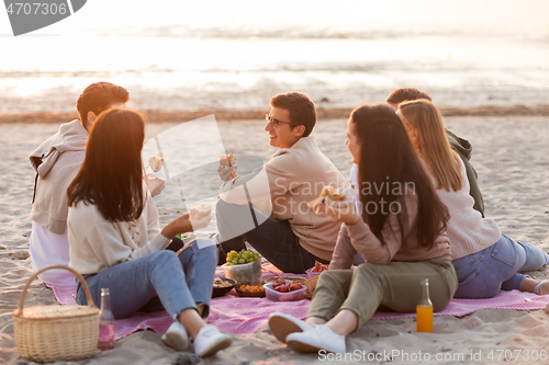 Image of happy friends eating sandwiches at picnic on beach