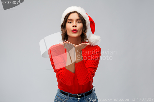 Image of happy young woman in santa hat sending air kiss