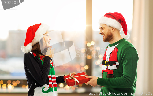 Image of happy couple in christmas sweaters with gift box