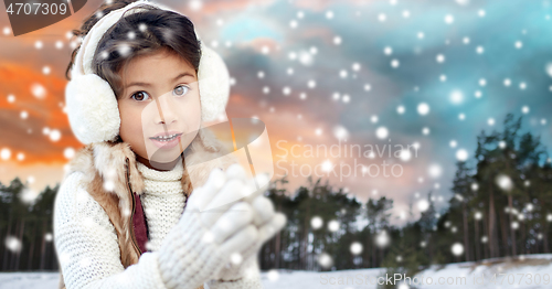 Image of happy little girl in earmuffs over winter forest