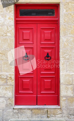 Image of Bright red wooden door of a house with black doorknob rings