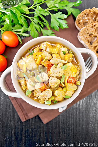 Image of Chicken with vegetables and peas in saucepan on dark board top