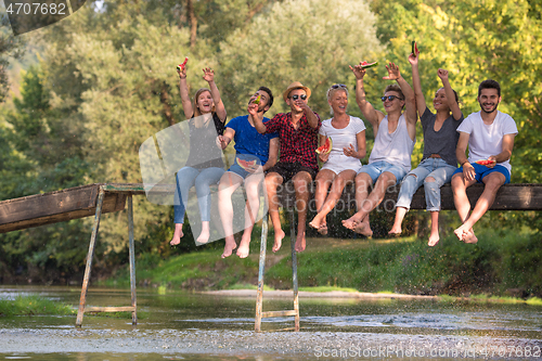 Image of friends enjoying watermelon while sitting on the wooden bridge