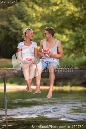 Image of couple enjoying watermelon while sitting on the wooden bridge