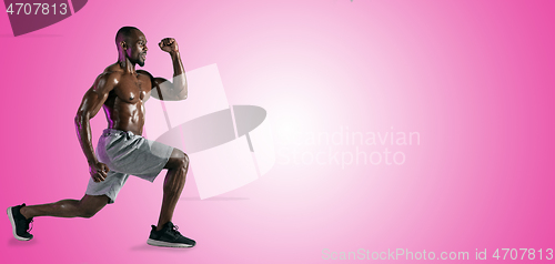 Image of Young african-american bodybuilder training over pink background