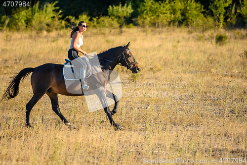 Image of Girl rides a horse across the field on a sunny day