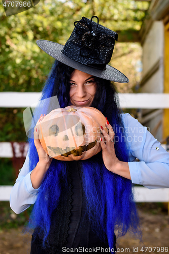 Image of A girl in a witch costume with blue hair is holding a pumpkin with a painted face