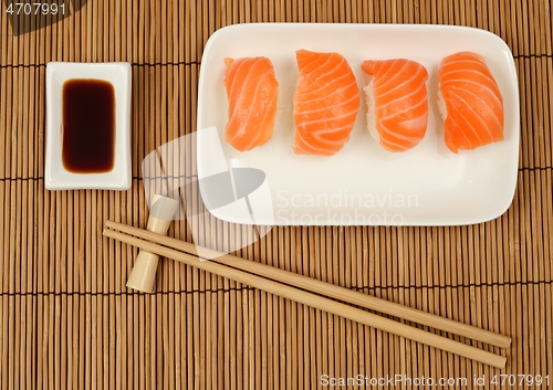 Image of chopsticks, soy sauce and sushi with salmon on the mat