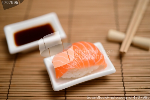 Image of chopsticks, soy sauce and sushi with salmon on the mat