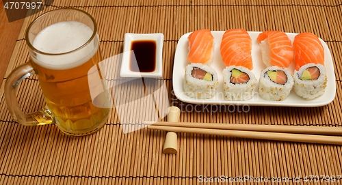 Image of chopsticks, soy sauce, sushi and glass of beer on the mat