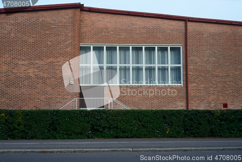 Image of facade of a brick building with a large window, deadpan photo