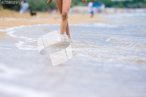 Image of Close-up of the girl\'s feet soiled in the sand, the girl walks along the coastal strip towards the camera