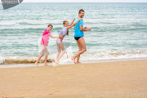 Image of A man and two daughters are happily running along the beach with a train