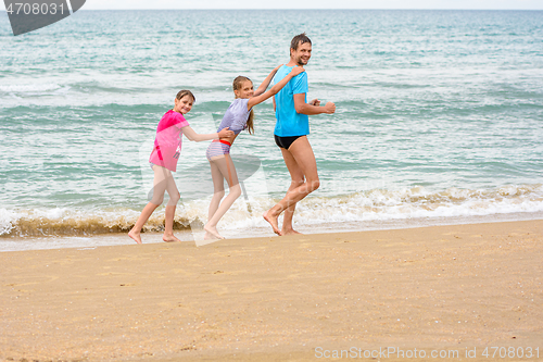 Image of A man and two daughters are happily running along the beach with a train