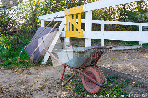 Image of Old wheelbarrow in the background of the corral for horses, in the background there are shovels
