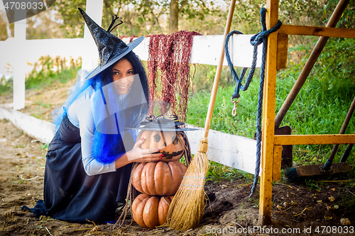 Image of A girl in a witch costume, celebrating Halloween, sat down by a pumpkin with a drawn malicious grimace