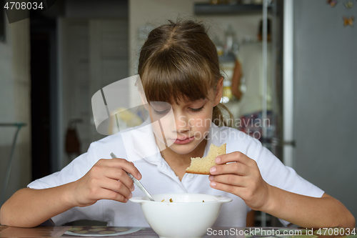 Image of A schoolgirl came from school and sat down to eat at the table in the kitchen at home