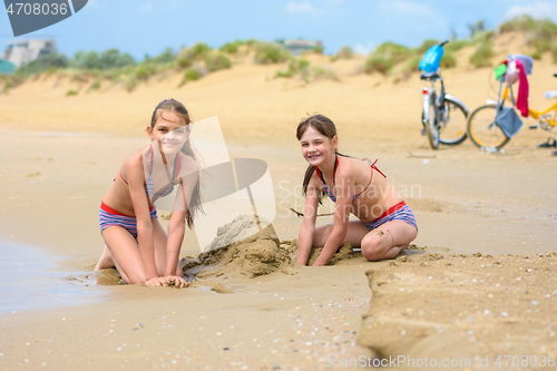 Image of Two girls build sand castles on the seashore, bicycles stand in the background