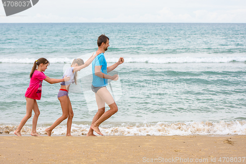 Image of Dad and two children have fun running a little train along the seashore