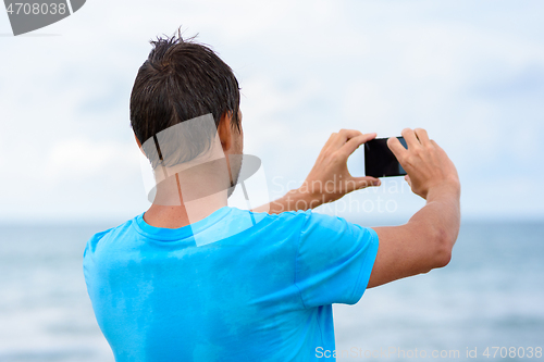 Image of Man photographs the seascape on a mobile phone