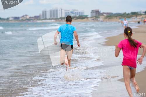 Image of A man runs along the beach, a girl runs after him, rear view