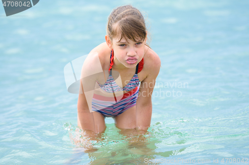 Image of A girl stands knee-deep in sea water, grimaces and shows her tongue