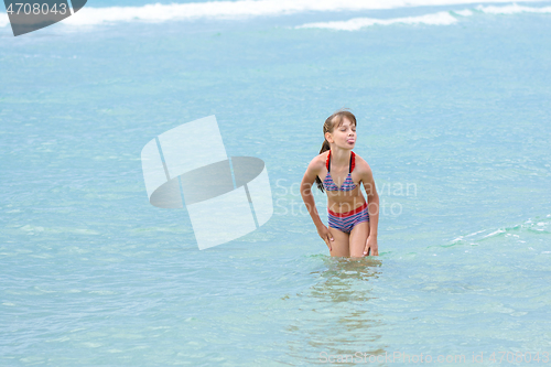 Image of A girl stands knee-deep in sea water, does not want to go out to bask and sticks out her tongue