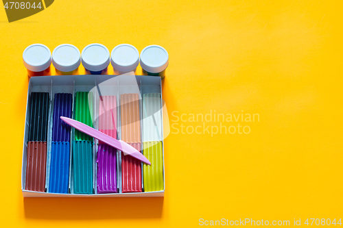 Image of On a yellow background lies a box with plasticine and paint