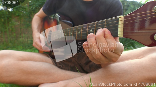 Image of Man sitting in the grass playing guitar