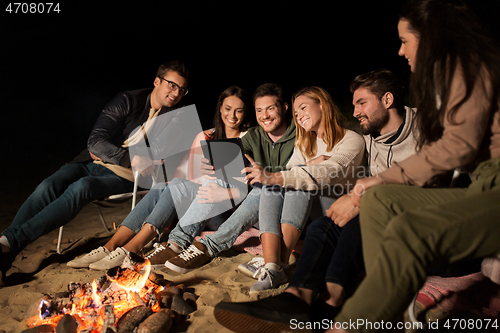 Image of friends with tablet pc at fire on beach at night