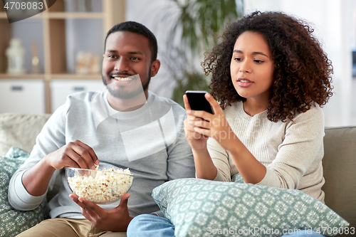 Image of african couple with popcorn watching tv at home