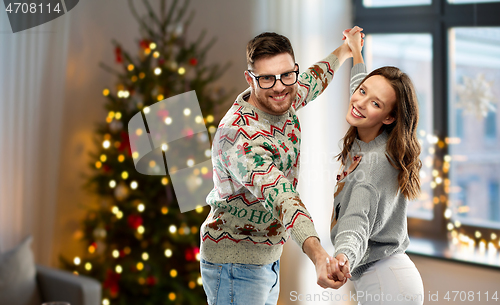 Image of couple dancing in christmas ugly sweaters at home