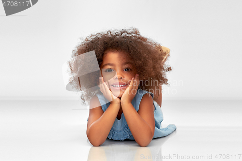 Image of happy little african american girl lying on floor