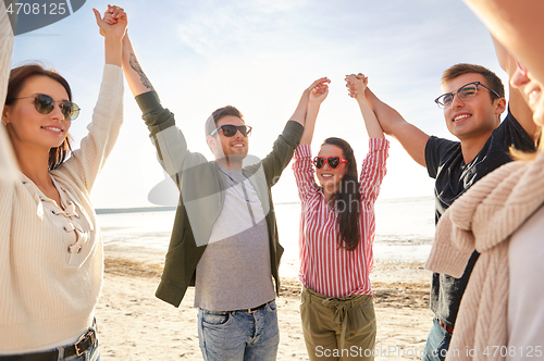 Image of happy friends holding hands on summer beach