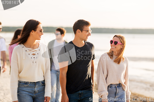 Image of happy friends walking along summer beach