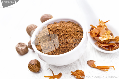 Image of Nutmeg round in bowl and mace in spoon on white board