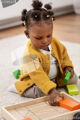 Image of african baby girl playing with toy blocks at home