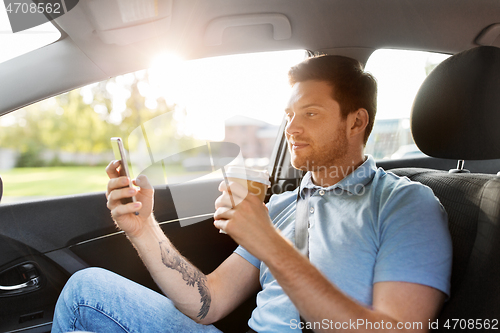 Image of passenger drinking coffee using smartphone in car