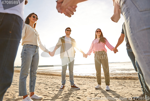 Image of happy friends holding hands on summer beach