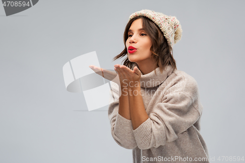 Image of young woman in knitted winter hat sending air kiss