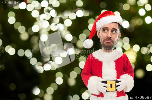 Image of sad man in santa claus costume over christmas tree