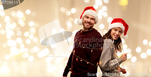 Image of couple in santa hats tied by christmas garland