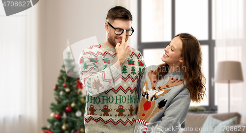 Image of happy couple in christmas ugly sweaters at home