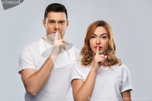 Image of happy couple in white t-shirts making hush gesture