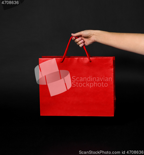 Image of hand holding red shopping bag on black background