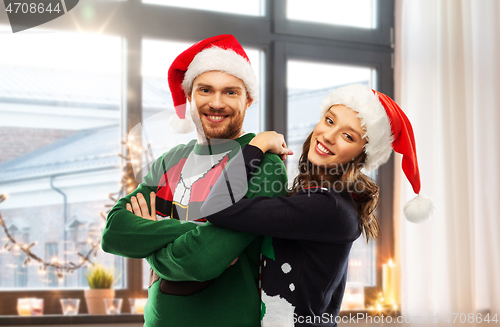 Image of happy couple in christmas sweaters and santa hats