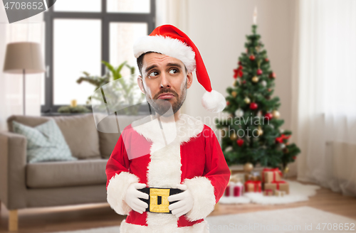 Image of sad man in santa claus costume over christmas tree