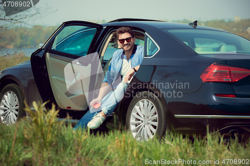 Image of Handsome smiling man sitting in his car with opened doors